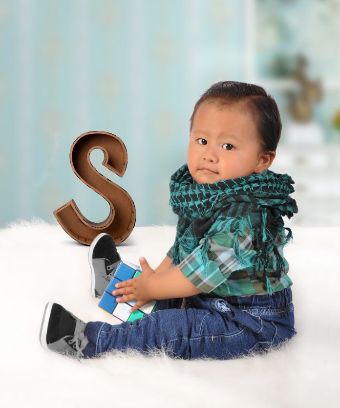 A baby sitting next to the letter S