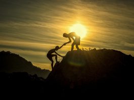 Man helping another man climb a mountain