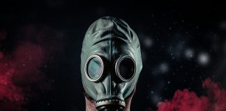 Man wearing gas mask with red smoke in the background.
